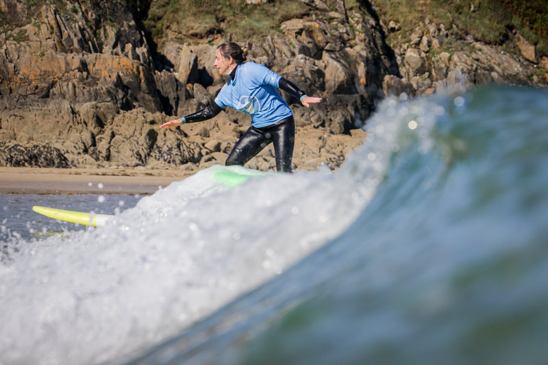 Apprendre à tenir son équilibre debout sur la planche, lors d'un cours de surf en famille.