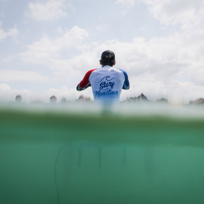 le moniteur de l'école Surf Harmony donne des consignes à l'eau lors d'un cours de surf.